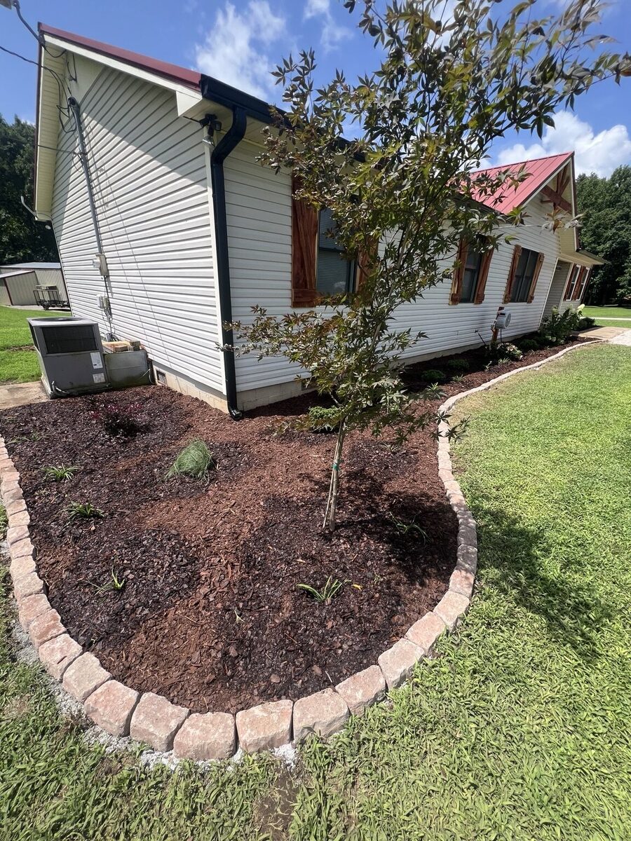 Curved landscape bed with fresh mulch, new plants, and stone edging completed by Bates Lawn Care