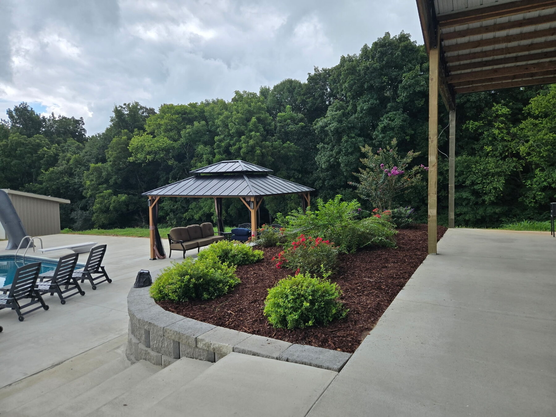 Finished poolside landscape with fresh mulch, flowering plants, shrubs, and retaining wall